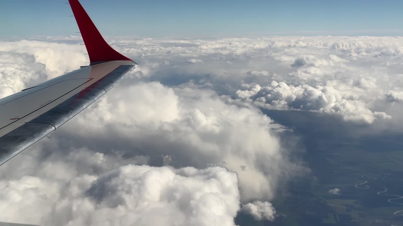 Vue depuis le hublot d'un avion d'Iași à Vienne montrant l'aile au-dessus d'une mer de nuages avec des aperçus du paysage en contrebas.