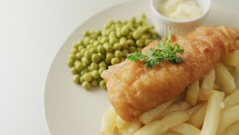 video de pescado, papas fritas y guisantes en un plato con salsa