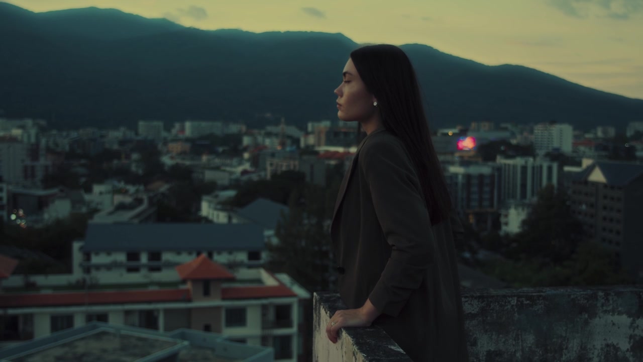 Young Woman Standing on Rooftop Overlooking City at Twilight