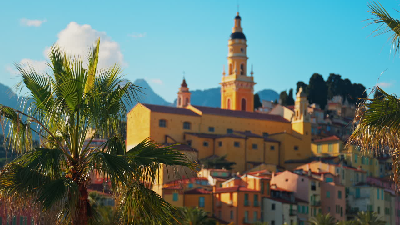 Distant view of the St Michel Basilica surrounded by colourful buildings and palm trees, Menton, France