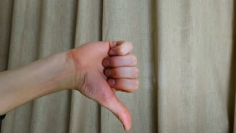 Dislike-thumbs-down-hand-symbol-on-a-brown-curtain-background,-closeup