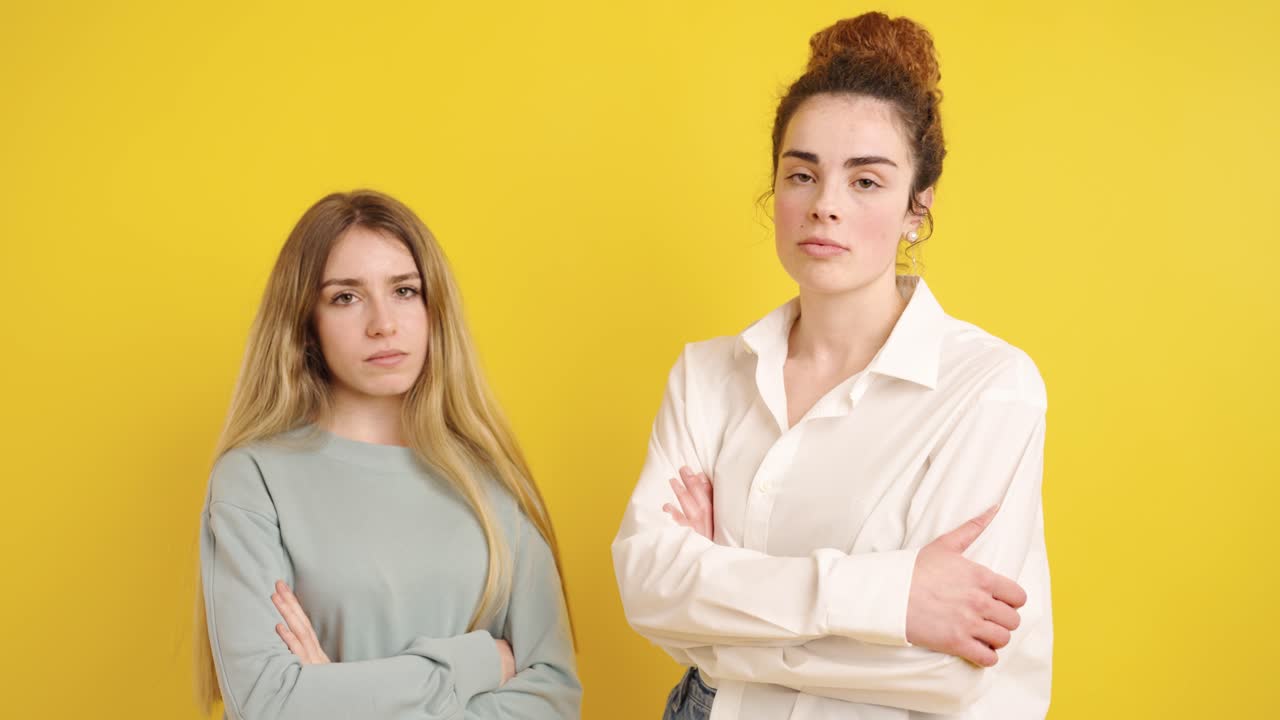 Young women posing with crossed arms on yellow background