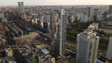 aerial flight of luxury mirror glass skyscraper with swimming pool on rooftop - epic city of buenos aires during sunset in background,argentina