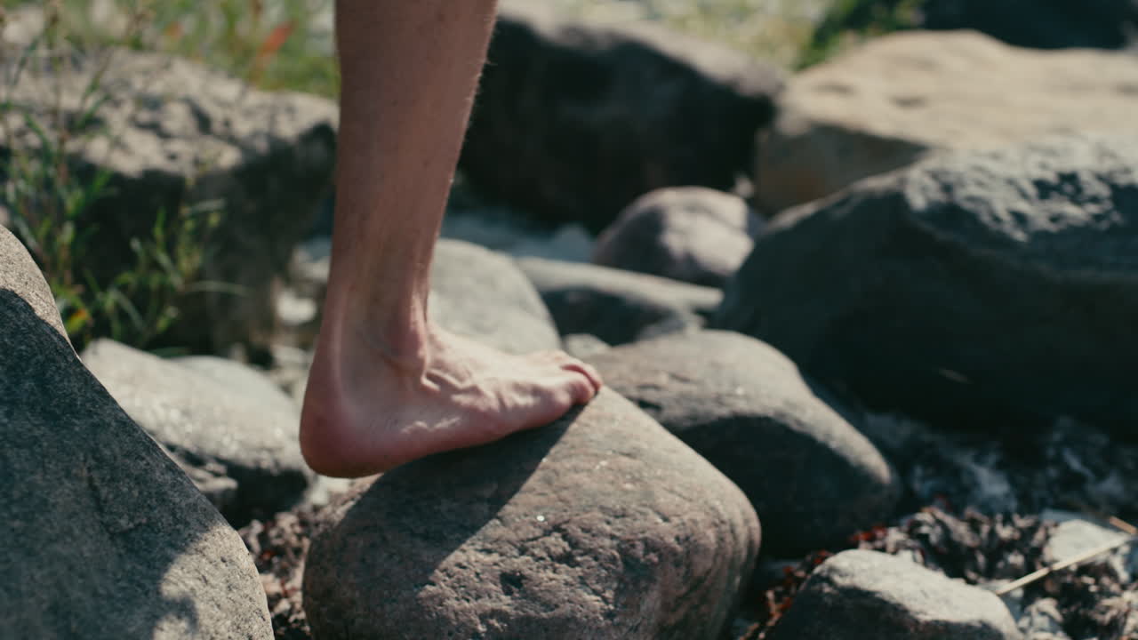 Man walking barefoot on rocks close to beach, close-up