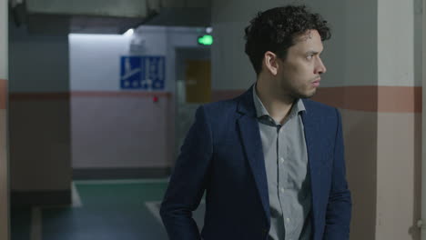 man in suit walks into underground parking and gets a feeling of danger ahead, looks around