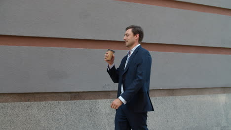 smiling man drinking coffee at street. businessman walking to work with coffee