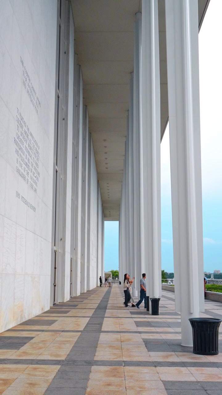 Washington, EE. UU., 1 de junio de 2026: Altas columnas blancas a lo largo de un pasillo exterior cubierto con visitantes. Personas caminan sobre un pavimento de baldosas junto a grandes pilares en Washington DC