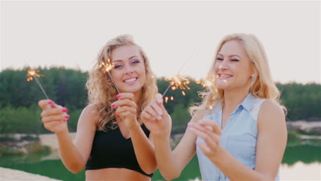 two attractive woman with sparklers laughing on the beach