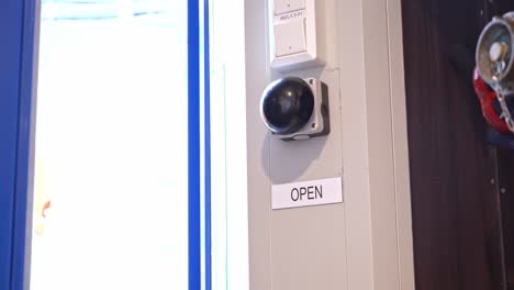 Hand-pushing-button-to-open-door-from-passenger-area-inside-ship---Static-clip-from-inside-passenger-area-with-bright-sunlight-outside-when-door-opens---Closeup-of-button-and-hand