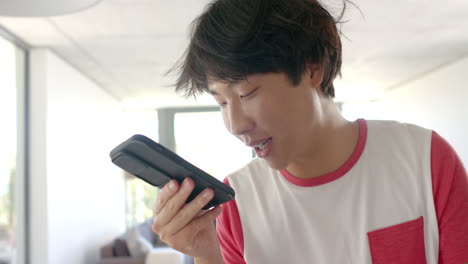 teenage asian boy talks into a phone at home in the kitchen