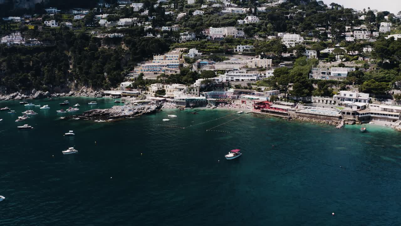Wide aerial shot pulling away from Capri, Italy's sunny shoreline