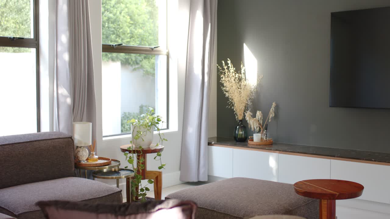La telecamera panoramica a destra, la luce del sole proietta chiazze sul divano componibile e sul pouf, rivelando l'arredamento.