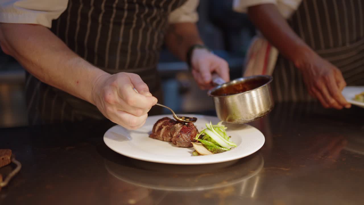View of a chefs hand pouring sauce over a perfectly cooked piece of meat as he plates up a meal in a fine dining restaurant