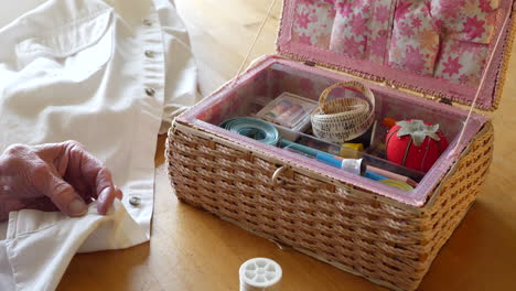 an old lady seamstress and her sewing kit as she cuts the thread of a button on a white dress shirt to be repaired