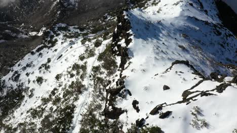 A-foot-path-with-footprints-in-the-snow-going-down-the-mountain-Pico-Ruivo-in-Madeira-with-its-foggy-and-cloudy-landscape