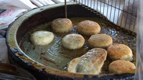 delicious xian bing cooking in the pan, a stall vendor flipping savoury minced pork meat pie pastry, deep-fried until golden brown with a crispy outside, close up shot of popular taiwanese street food