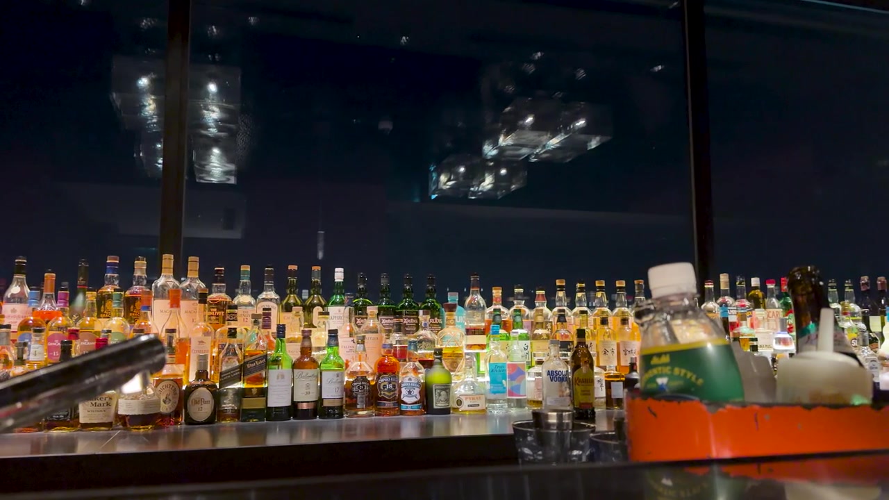 Panorámica lenta cinematográfica a través de un bar de lujo con diversas botellas de whisky y herramientas de cóctel