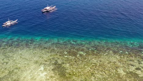 Philippines-beach-with-catamaran-traditional-fishing-and-diving-boats-near-the-shore,-Aerial-flyover-reveal-shot