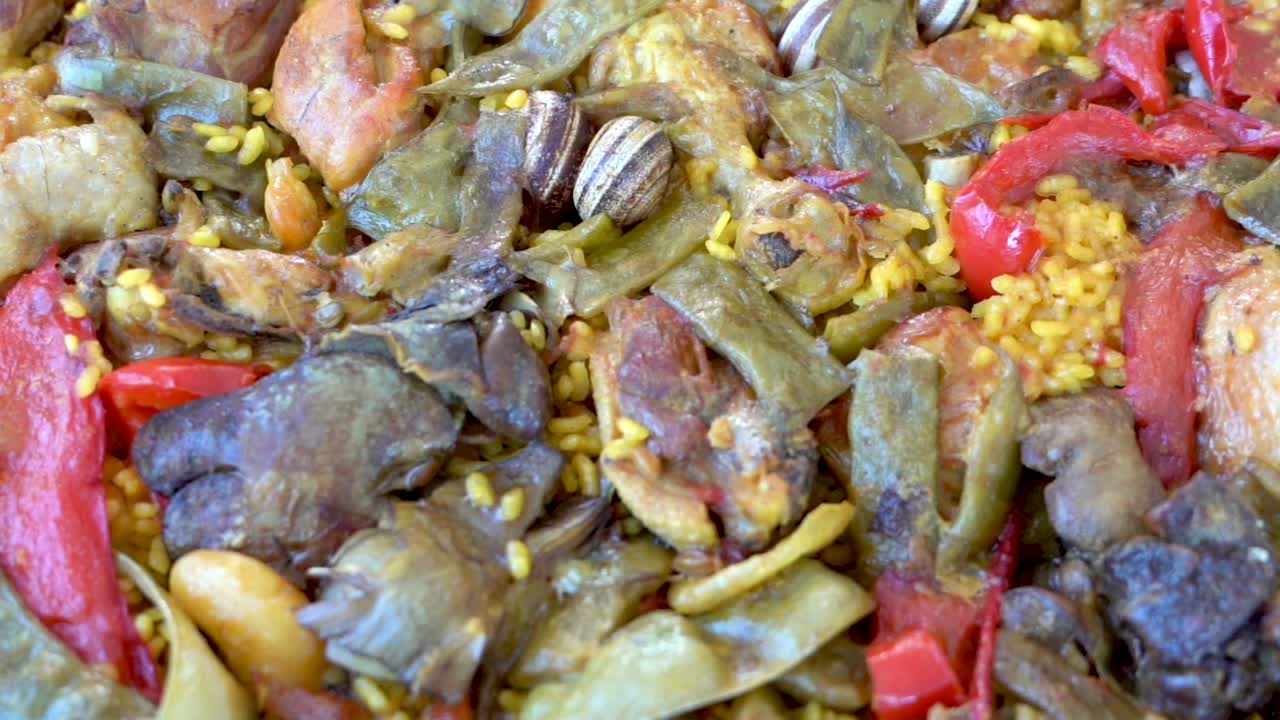 Primer plano de un plato de paella española terminado, relleno de mariscos y otras carnes, grabado con un paneo de derecha a izquierda