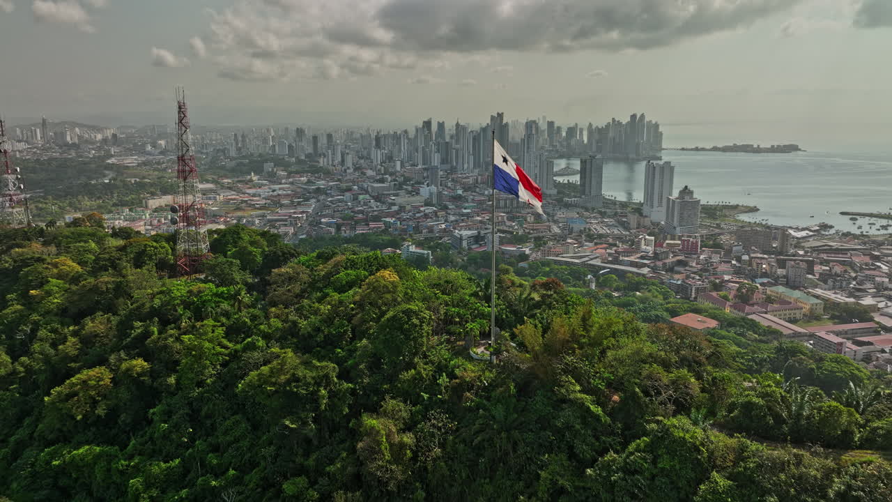 Panama City Aerial v67 cinematic low level flyover ancon hill with wind blowing the national flag on hilltop with coastal downtown cityscape in the background - Shot with Mavic 3 Cine - March 2022