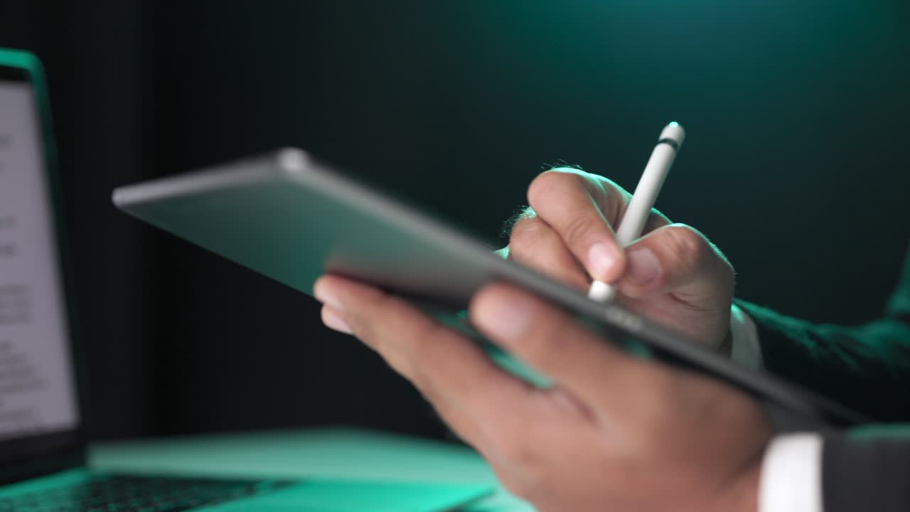 Electronic signature with green light. Businessman signing a business contract with stylus pen on tablet at night. Man signing contract on tablet at office. Business and technology concept.