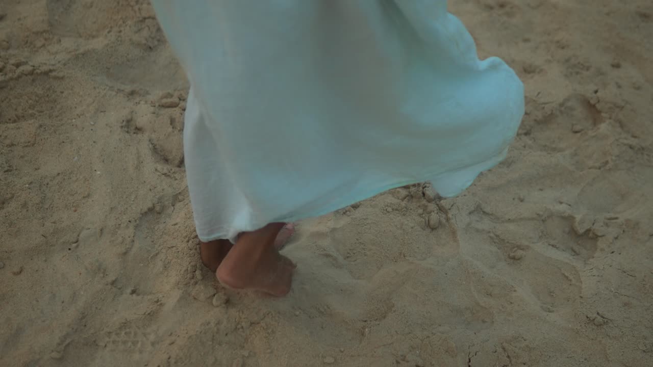 Barfodet person på sandstrand i skumringen løfter forsigtigt en blå kjole