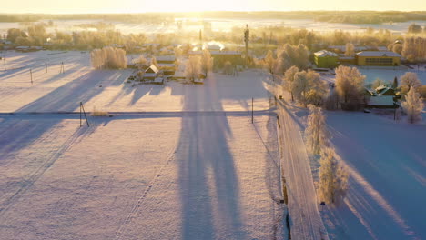 Snow-covered-countryside-aerial-view-flying-over-patchwork-farmland-towards-rural-European-ranch