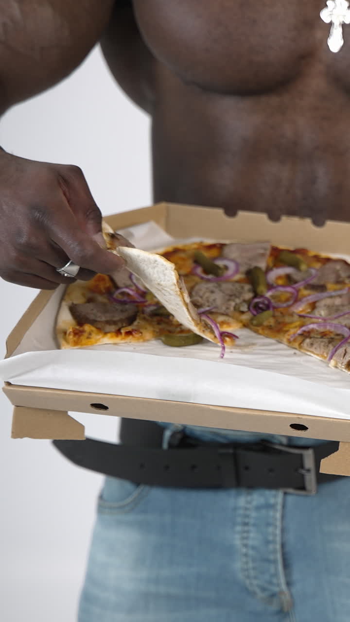 Male torso of african athlete. Young muscular african man with naked torso eating pizza in studio