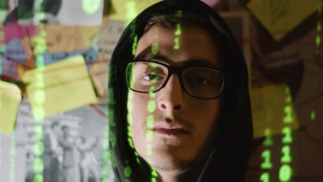 young male hacker in hood looking at camera with binary code reflection on his face