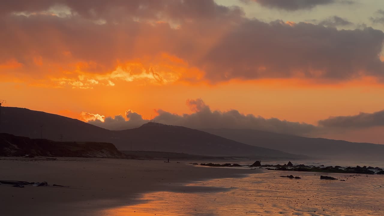 Il sole che splende intensamente da dietro le colline durante il tramonto, con una spiaggia calma in primo piano.