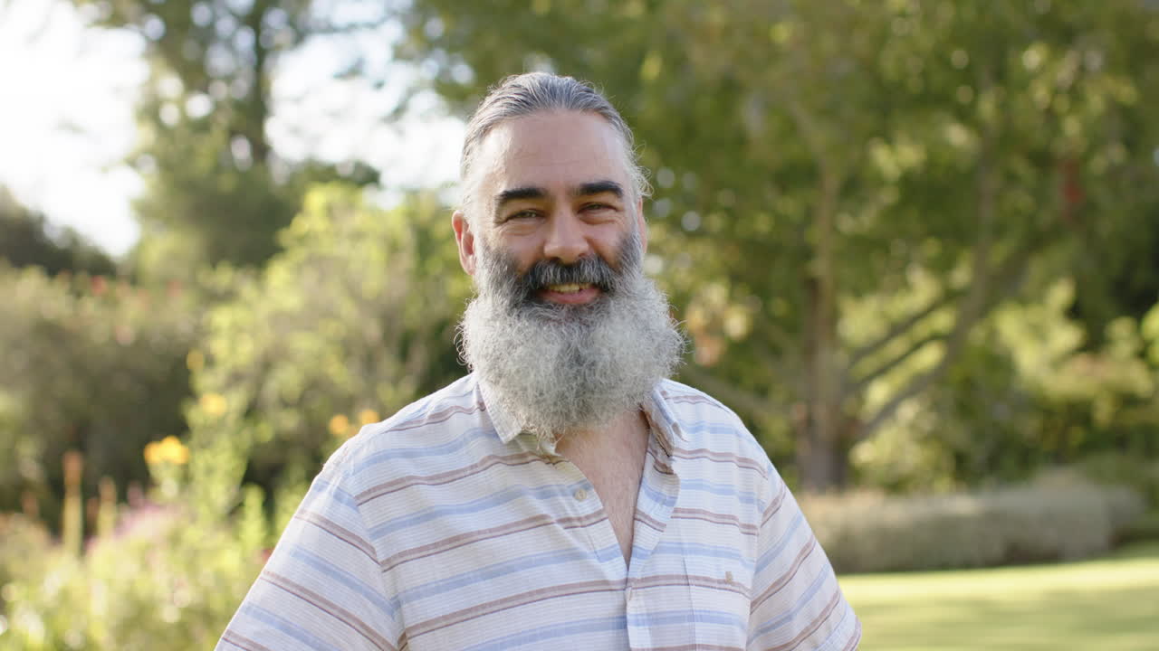 Smiling man with gray beard standing outdoors in casual shirt, enjoying nature