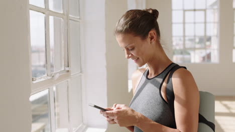 hermosa mujer de yoga usando mensajes de texto de teléfonos inteligentes compartiendo prácticas de entrenamiento en las redes sociales mirando por la ventana planificando con anticipación en el estudio de bienestar