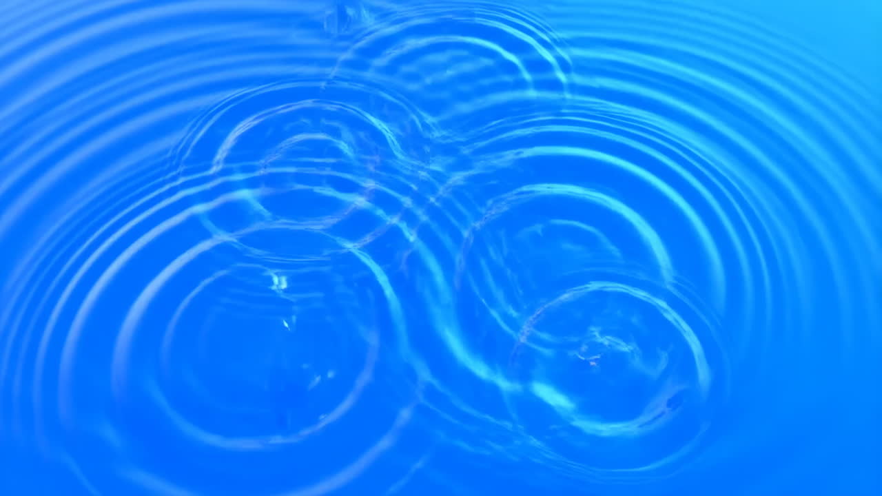 Primo piano di increspature blu nell'acqua causate da gocce che cadono