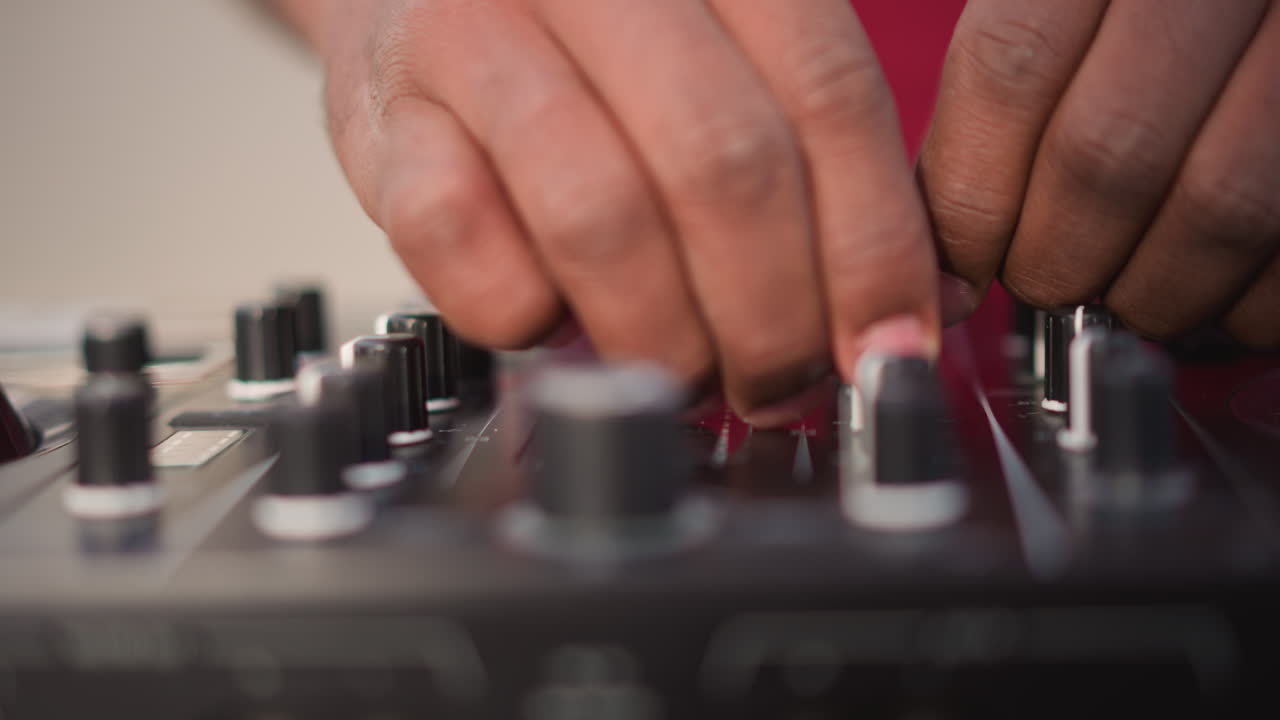 black dj hands on mixer adjusting knobs and faders, cueing tracks and dialing equalizer, closeup focus on fingers performing precise scratch and tempo control on controller, warm studio lighting