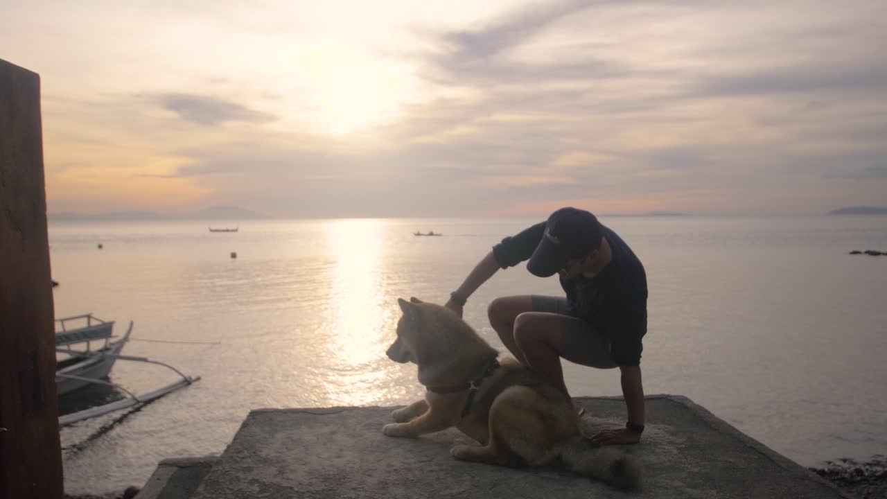 vídeo em câmera lenta de homem abraçando cachorro em uma plataforma com pôr do sol ao fundo