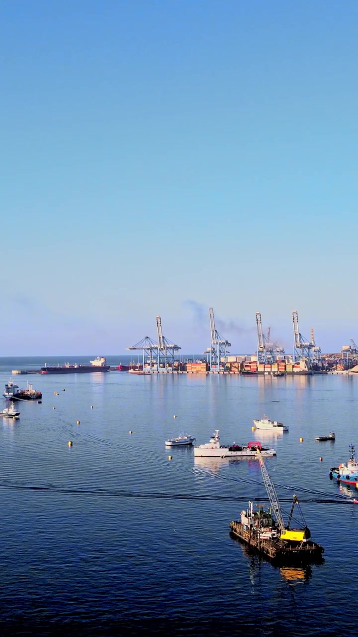 Un video vertical captura una vista aérea de un puerto bullicioso con grúas, barcos y aguas tranquilas a plena luz del día, ideal para historias sociales móviles.