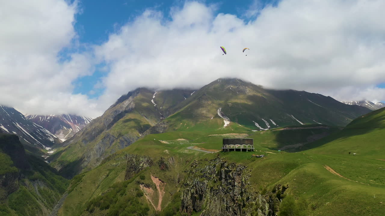 toma cinematográfica de drones de las montañas del cáucaso con el arco de la amistad de los pueblos en la distancia con personas en parapente