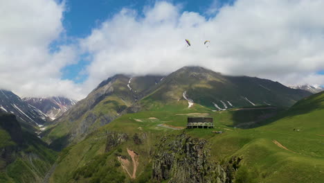 cinematic drone shot of the caucasus mountains with the arch of friendship of peoples in the distance with people paragliding