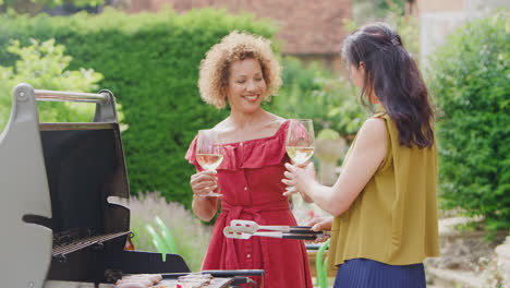 two mature female friends cooking outdoor barbeque and drinking wine at home