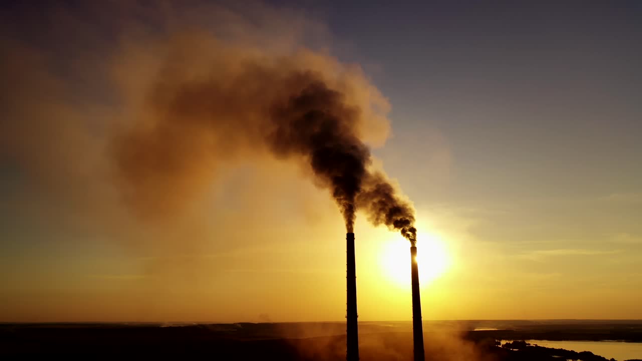 Dark smoke from factory. Industrial pipes of manufacture pollute the atmosphere at sunset. Toxic smoke in the air. Ecological problems.