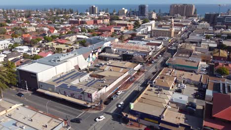 a sunny day in glenelg, south australia. this drone shot shows jetty road, the main street of the beachside suburb. people and cars go about their days in this popular australian destination.