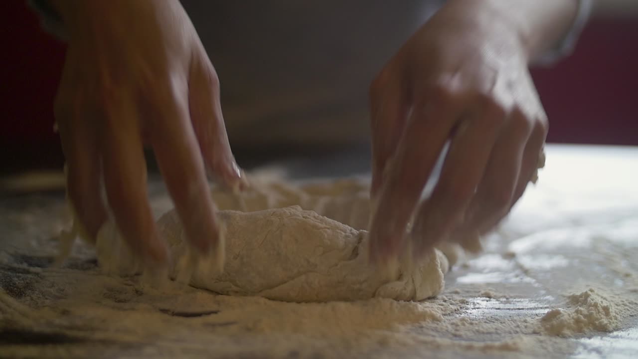 Mani di donna che impastano pizza su un tavolo di marmo pieno di farina