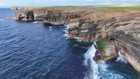 aerial view of ocean waves crashing under cliffs on coastline of scotland uk, yesnaby vista point of sunny day