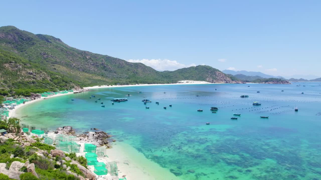 Panoramic view of a pristine beach with turquoise waters, white sand, and lush green mountains under a sunny blue sky