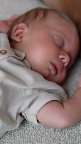 adorable newborn sleeps on the bed holding hands up. male hands stroke child's belly. close up. vertical video