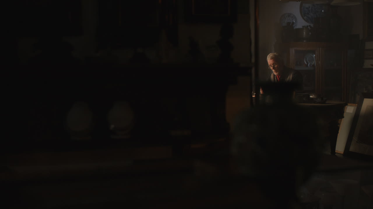 Older passionate man evaluates an old watch in his office at night