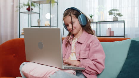 child girl in headphones using laptop listens to music or lesson distance learning education at home