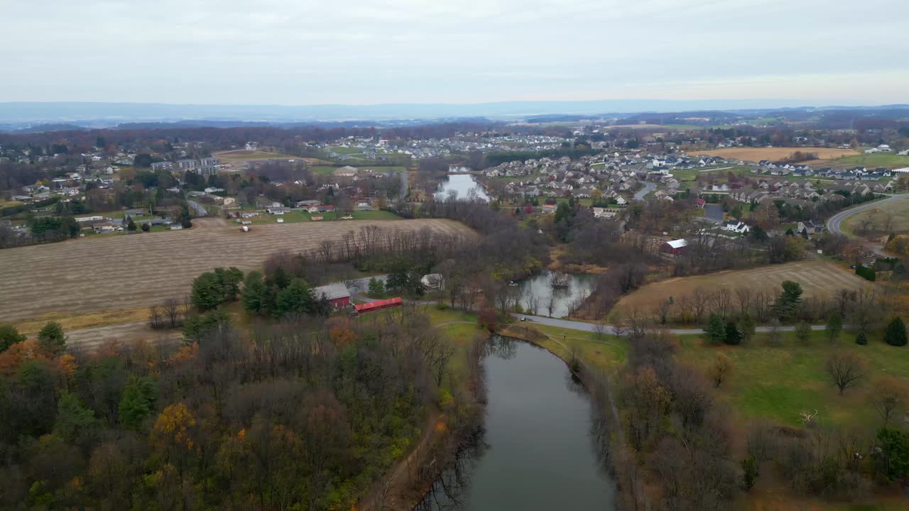 Aerial drone video of a lake and barn with a neighborhood and farm fields in the distance