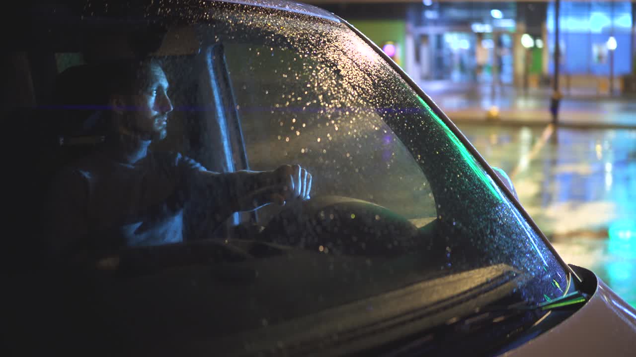 비가 오는 저녁에 차에 앉아 있는 젊은 남자