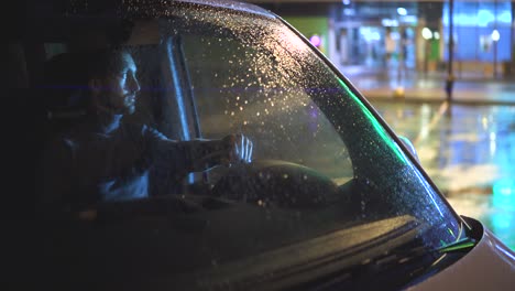 el joven sentado en el coche en la noche lluviosa